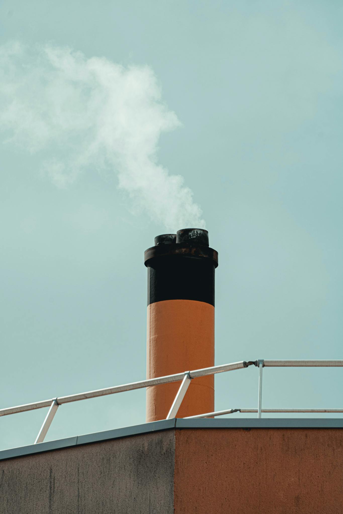 A rooftop chimney releasing smoke into a clear blue sky, highlighting industrial pollution.